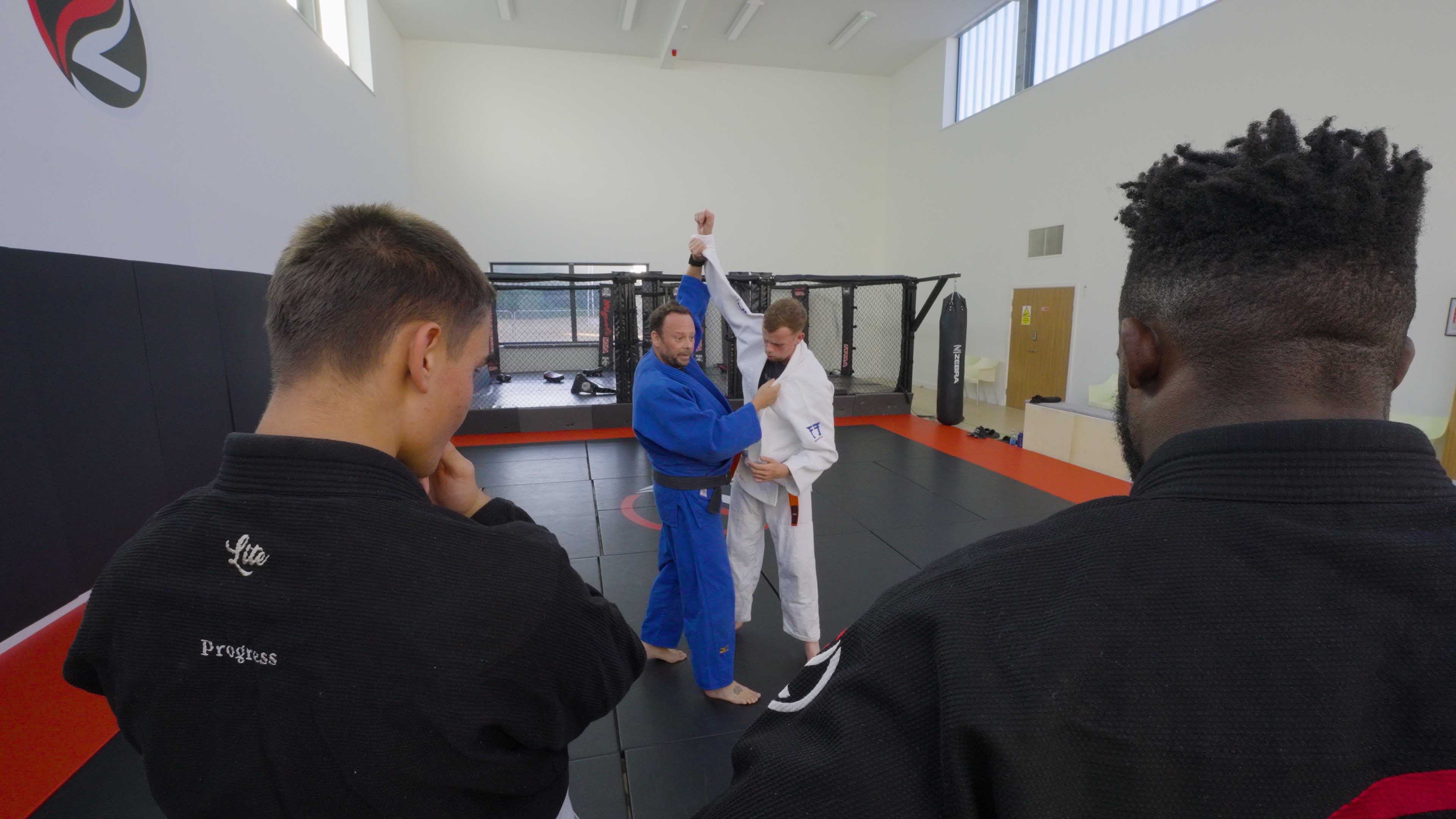 Judo coach demonstrating a grip and throw setup to students at Zilla Training
